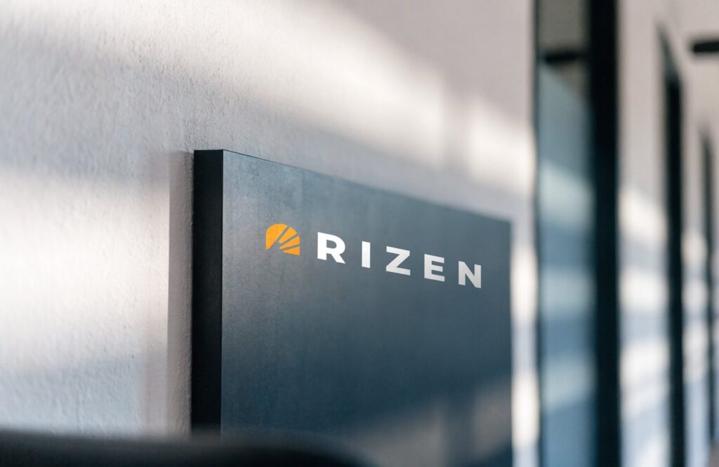 Dimensional Rizen wall sign, orange icon and white wordmark on a dark panel